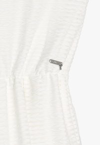 Vit klänning med ett texturerat mönster och rynkdetalj. Har en silver dragkedjeförslutning med märkeslogotyp på sidan.