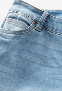 Tela de mezclilla de color azul claro con una textura suave, que presenta costuras naranjas en contraste y múltiples bolsillos. Incluye una cintura con un botón.