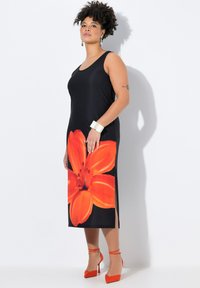 Musta hihaton mekko, jossa on suuri punakirjava liljatulostus alaosassa ja sivureikien leikattu. Yhdistetty oransseihin korkokenkiin ja hopeiseen rannerenkaaseen.