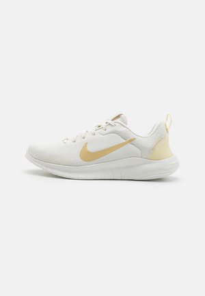 Hvid og beige Nike løbesko med mesh-overside, polstret sål og snørelukning, vist fra siden på en lys baggrund.