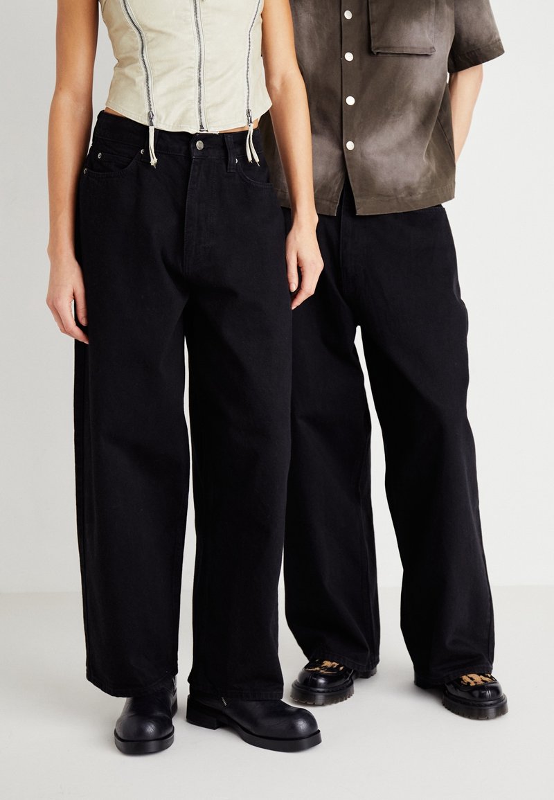 Černé široké džíny s vysokým pasem, s předními kapsami. Kombinovány s lehkým crop topem a tmavou košilí s krátkým rukávem. Černé boty.