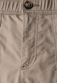 I pantaloni beige in cotone presentano una texture liscia, una tasca frontale prominente e un bottone rotondo e decorato con quattro fori per il fissaggio.