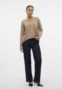 Pull en coton beige clair avec une coupe décontractée et des manches longues, associé à un jean droit bleu marine et des escarpins noirs.