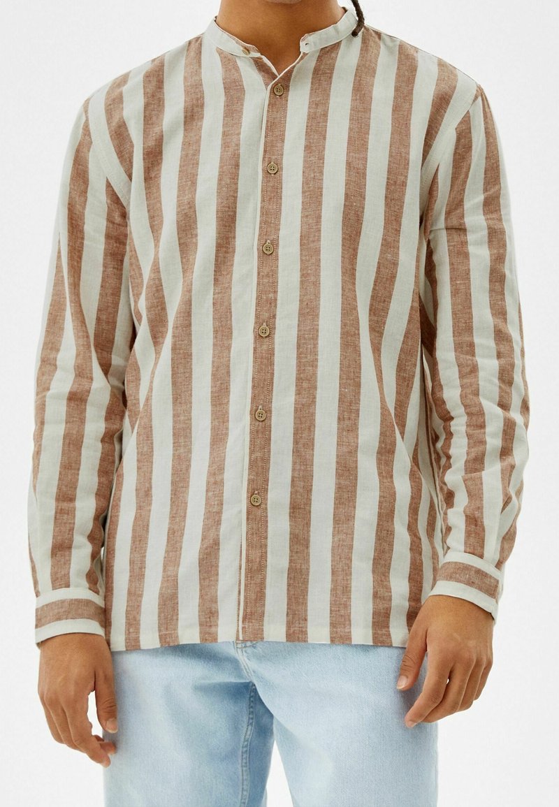 Långärmad skjorta med vertikala ränder i ljusbrun och off-white, tillverkad av ett ventilerande tyg. Knäppning framtill med ståkrage.