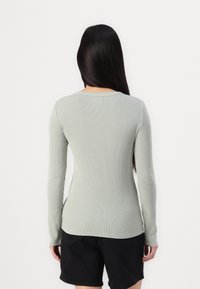 Langsleeve geribbelde top van zacht lichtgroen materiaal, met een ronde halslijn en zijsplitten, gecombineerd met zwarte shorts.