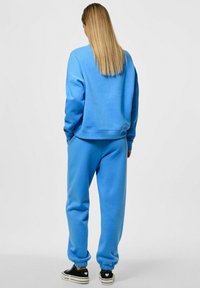Sudadera de algodón azul y joggers a juego, con un corte relajado y puños de canalé. Zapatillas negras con acentos blancos completan el atuendo.