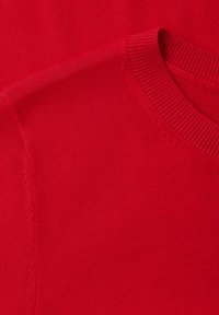 Gros plan d'un pull rouge à col rond en maille montrant les coutures détaillées sur le col et la zone des épaules.