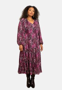 Šaty s květinovým potiskem v odstínech fialové a růžové, s dlouhými rukávy, výstřihem do V a sukni ve vrstvách. Nosené s černými kozačkami po kolena.