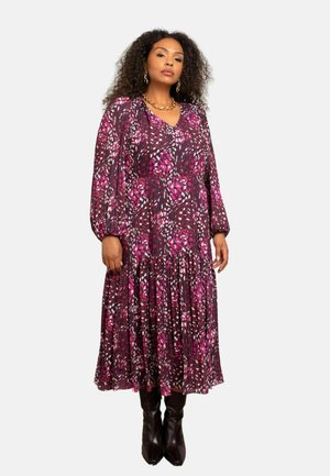 Bloemenprint jurk in tinten paars en roze, met lange mouwen, een V-hals en een gelaagd rokje. Draagt een paar zwarte laarzen tot de knie.