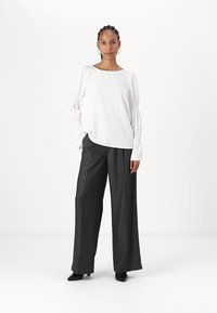 Blusa bianca a maniche lunghe con dettagli arricciati e vestibilità rilassata, abbinata a pantaloni grigi a vita alta e a gamba larga realizzati in tessuto testurizzato.