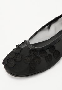 Black ballet flat featuring a mesh upper with textured floral appliqués, round toe design, and smooth black trim at the opening.