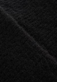 Schwarzer, strukturierter Stoff mit einer weichen, samtigen Oberfläche, die unterschiedliche Dicke und einen dezenten Glanz aufweist. Er ist dicht gewebt und wirkt warm.