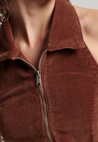 Brauner Corduroy-Ärmelloser Top mit Kragen und Reißverschluss vorne. Hat eine weiche Textur und eine figurbetonte Passform.