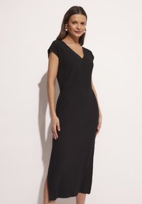 Czarna prążkowana sukienka midi z dekoltem w serek i kr�ótkimi rękawami, z bocznymi rozcięciami dla swobody ruchów i dopasowanym krojem.