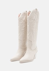 Bottes de cowboy en cuir blanc avec des bouts pointus, des motifs de couture complexes et un large talon. Présente un design décoratif sur la tige.