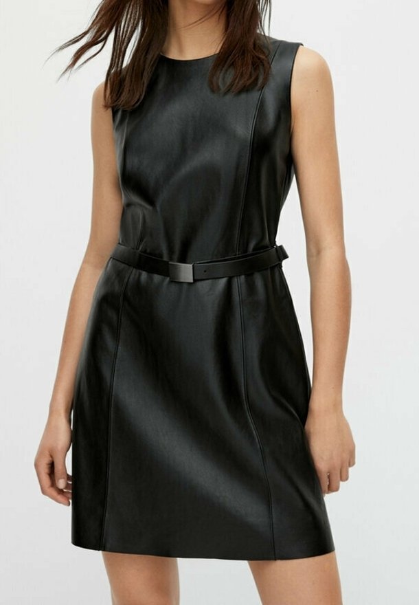 Robe en cuir noire sans manches avec une ceinture cintrée à la taille portée par une personne debout aux cheveux longs.