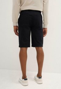 Pantaloni shorts neri in misto cotone, con due tasche posteriori, una vestibilità rilassata e un orlo semplice. Indossati con sneaker bianche e un maglione leggero.