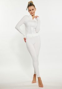 Completo sportivo bianco composto da giacca aderente con maniche lunghe e zip, abbinato a leggings coordinati. Il tessuto morbido e il design senza cuciture aumentano il comfort.