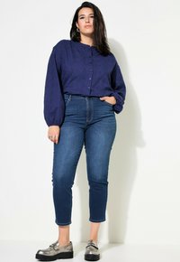 Marinblå skjorta med knappar och strukturerat mönster, i kombination med högmidjade blåjeans. Silverfärgade loafers med tjocka svarta sulor.