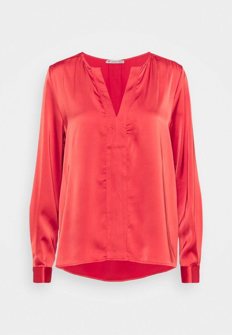 Blouse rouge en satin à manches longues avec un col en V, coupe ample et poignets boutonnés, présentée sur fond blanc uni.