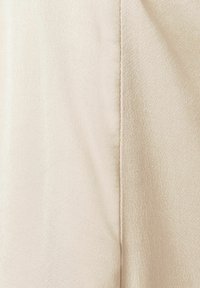 Tissu beige clair avec une texture lisse et légèrement brillante ; présente une couture droite le long d'un bord.