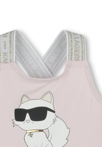Haut de bain rose avec des bretelles blanches entrecroisées ornées d'accents dorés. Le design avant inclut un chat blanc en cartoon portant des lunettes de soleil.
