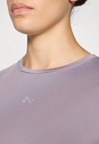 Light purple athletic shirt made of smooth, stretchy fabric with a crew neckline and a subtle logo detail on the front.