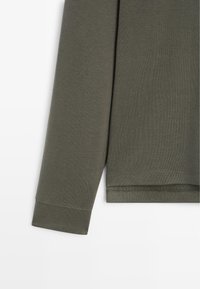 Langärmliges Hemd aus olivgrünem Baumwollstoff, mit glatter Textur, gerippten Bündchen und geradem Saum mit sauberem Nähten.