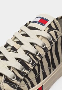 Χαμηλό αθλητικό παπούτσι με μαύρες και μπεζ ρίγες ζέβρας, λευκά κορδόνια και λογότυπο Tommy Jeans στη γλώσσα και στη σόλα.