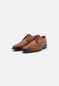 Scarpe in pelle marrone con un design perforato, punta affilata e dettagli brogue. Presentano lacci marroni e una suola nera.