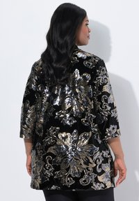 Giacca in velluto nero con un design floreale in paillettes dorate e argentate, maniche a tre quarti, lunghezza media e vestibilità morbida.