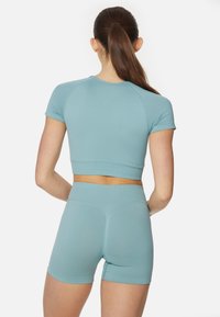 Světle modrý fitness set obsahující přiléhavý krátký rukáv crop top a šortky s vysokým pasem. Hladká textura s minimem švů a těsným střihem.