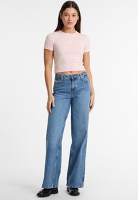 Light pink, short-sleeve cropped t-shirt with a white star logo, paired with wide-leg blue denim jeans and black shoes. Smooth texture.