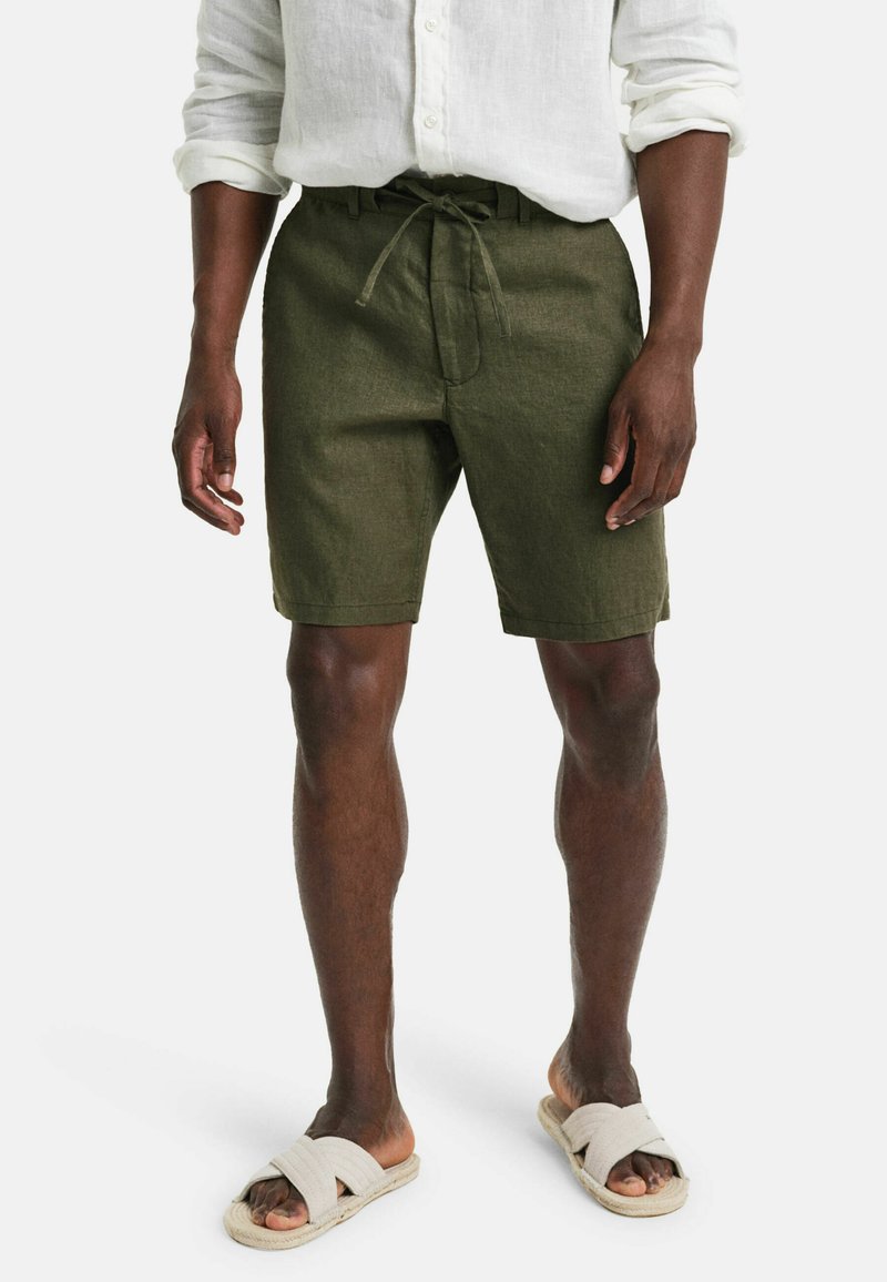 Olivgrüne Leinen-Shorts mit einem Kordelzug und Seitentaschen. Kombiniert mit beigen Rutschsandalen für einen lässigen Look.