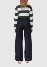 Gestreiftes langärmliges Hemd in Grün und Weiß, kombiniert mit dunkelblauen, weiten Jeans. Schlichte Rückansicht, die einen lässigen Look präsentiert.