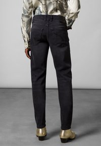 Jeans negros de mezclilla con corte de pierna recta, con bolsillos traseros y etiqueta en la pretina; combinados con botas de tacón brillantes doradas.