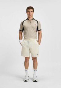 Beige kortærmet top med sorte detaljer og lynlås ved kraven, kombineret med cremede shorts. Mærket med "BOSS" på toppen og shortsene. Hvide sokker og sneakers.