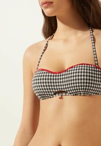 Top de bikini a cuadros blancos y negros con un borde rojo con forma de ondas, tirantes ajustables y un pequeño detalle de cerezas en el centro.