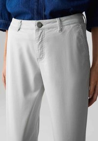 Pantalon gris clair avec une texture lisse, doté d'une poche avant, de coutures discrètes et d'un bouton en métal à la taille.