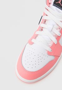 Pantof sport roz și alb cu partea superioară din piele netedă, vârf perforat, șireturi și logo negru. Talpă de cauciuc cu un accent roz contrastant.