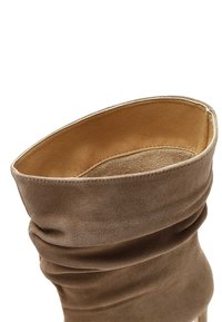 Stivaletto alla caviglia in suede marrone con un design morbido, texture morbida e rivestimento in pelle liscia. Presenta un'apertura arrotondata e dettagli di cucitura sottili.