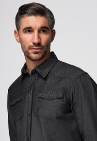 Chemise boutonnée gris foncé en tissu texturé, avec deux poches poitrine à rabats, col pointu et détails de couture subtils.