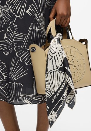 Sac à main beige avec un design perforé, comportant deux poignées supérieures. Un foulard noir et blanc à motifs est noué à l'une des poignées.