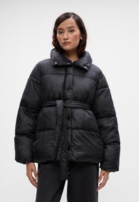 Casaco puffer preto com um grande colarinho, cintura cingida e tecido brilhante. Apresenta botões e um padrão acolchoado para isolamento.