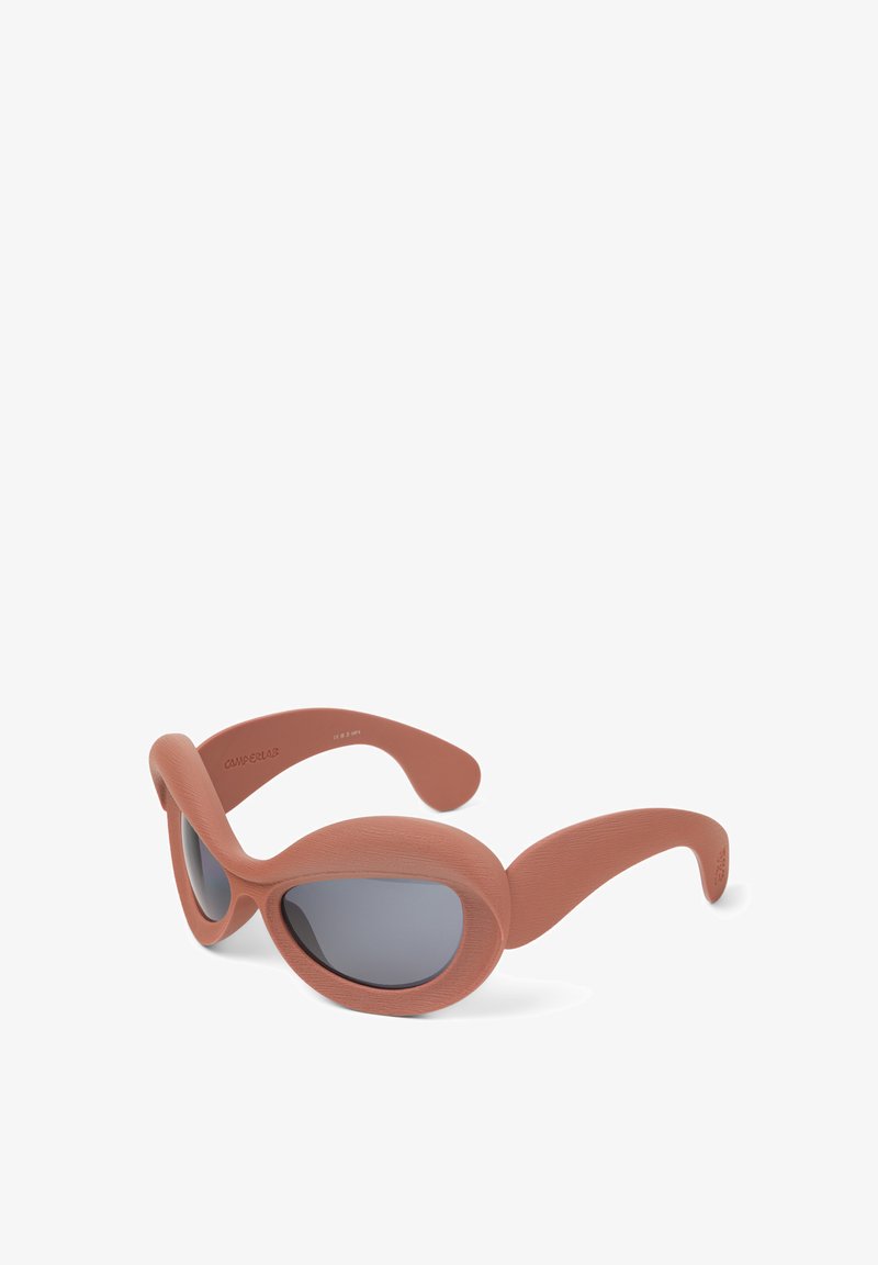 Oversized sunglasses with a matte terracotta frame, rounded shape, and gray tinted lenses. Features thick sides and a textured finish.