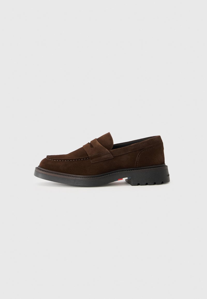 Mocassins en daim brun avec un bout arrondi, des détails à double bande et une semelle en caoutchouc noir présentant des rainures texturées.