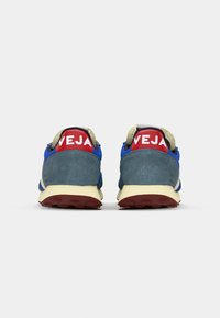 Blå og grå sneakers med røde hælflapper, beige snørebånd og gummisåler. Har en blanding av materialer inkludert semsket skinn og mesh.