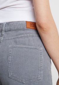 Grå kordflorsbyxor med vertikala räfflor, med en brun läderetikett med "BDG" på midjan och en synlig bakficka.