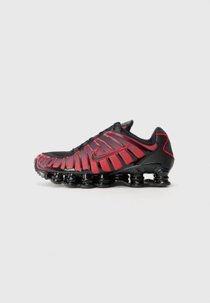 Czarno-czerwony but sportowy z widocznymi sprężynowymi elementami podeszwy i logo Nike z boku.