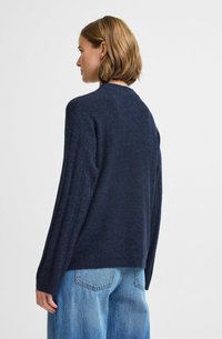 Maglione a maglia blu navy con vestibilità rilassata, polsini a coste e colletto rotondo, abbinato a jeans in denim azzurro. Tessuto morbido.